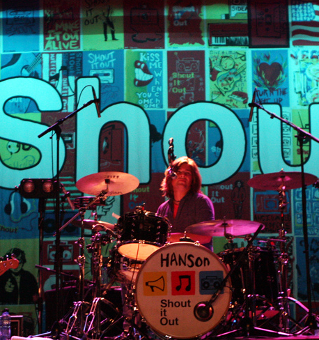 Drummer performing live with 'Shout Out' drum kit and backdrop.