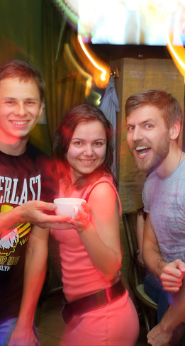 Three friends smiling and holding a cup at a lively gathering.